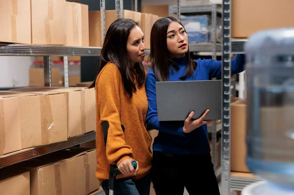 two workers organizing inventory in a warehouse with shelves of boxes